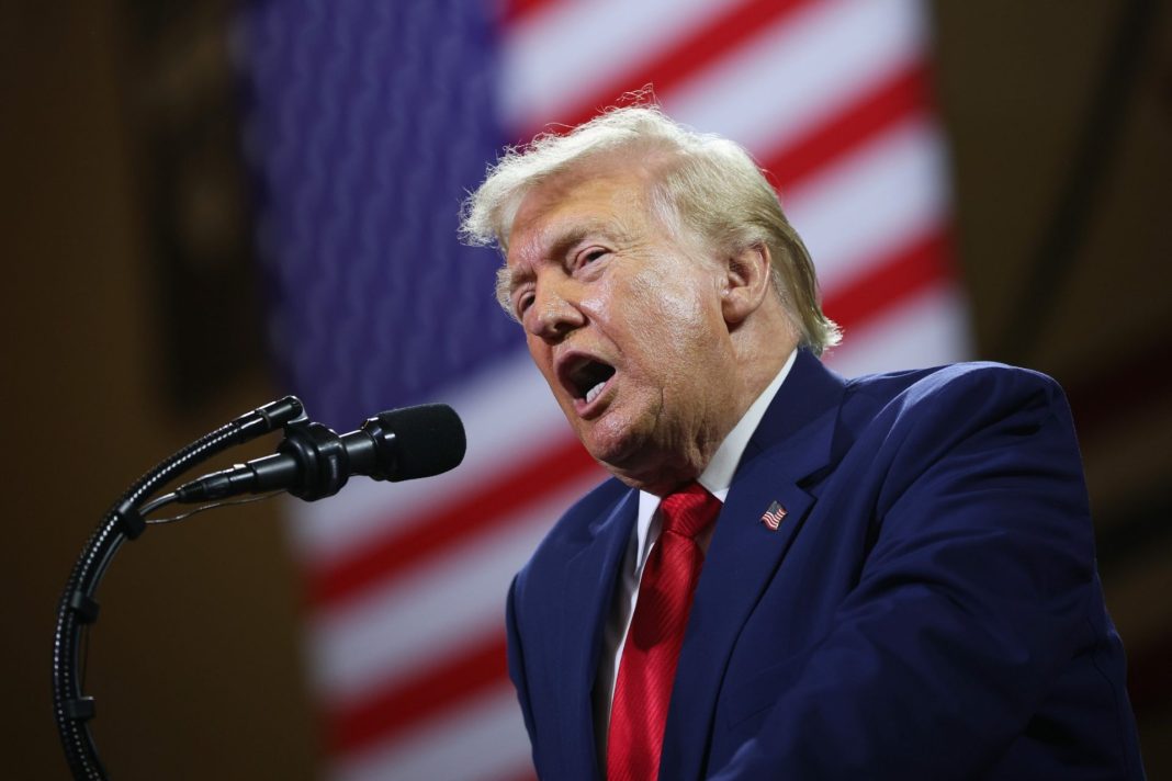 Donald Trump hovoří do mikrofonu před americkou vlajkou