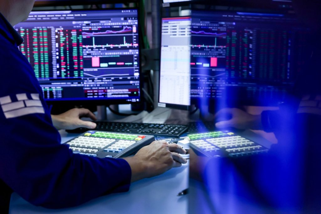 Obchodník pracuje u několika monitorů s burzovními daty a cenovými grafy