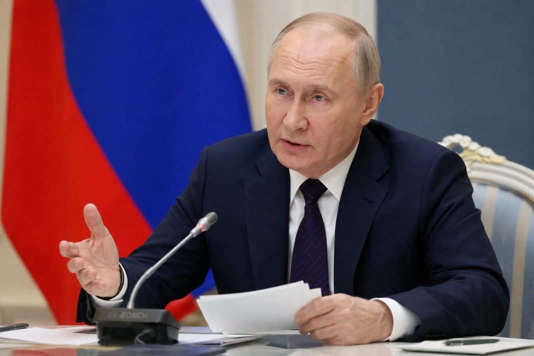 Vladimir Putin sedí u jednacího stolu před ruskou vlajkou