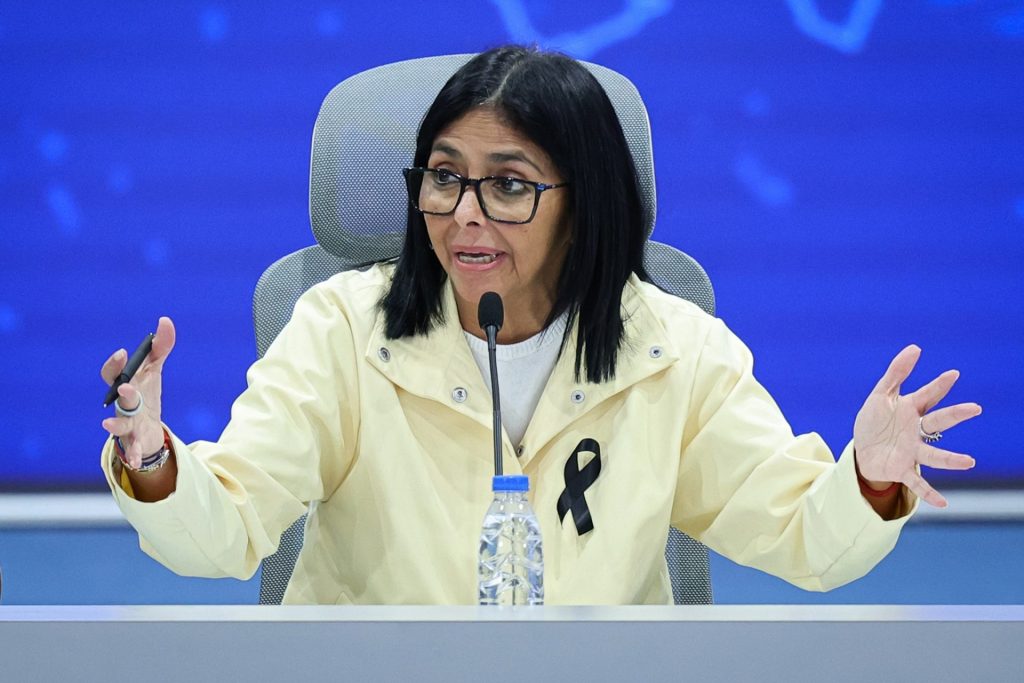 Žena v brýlích hovoří u mikrofonu a gestikuluje rukama