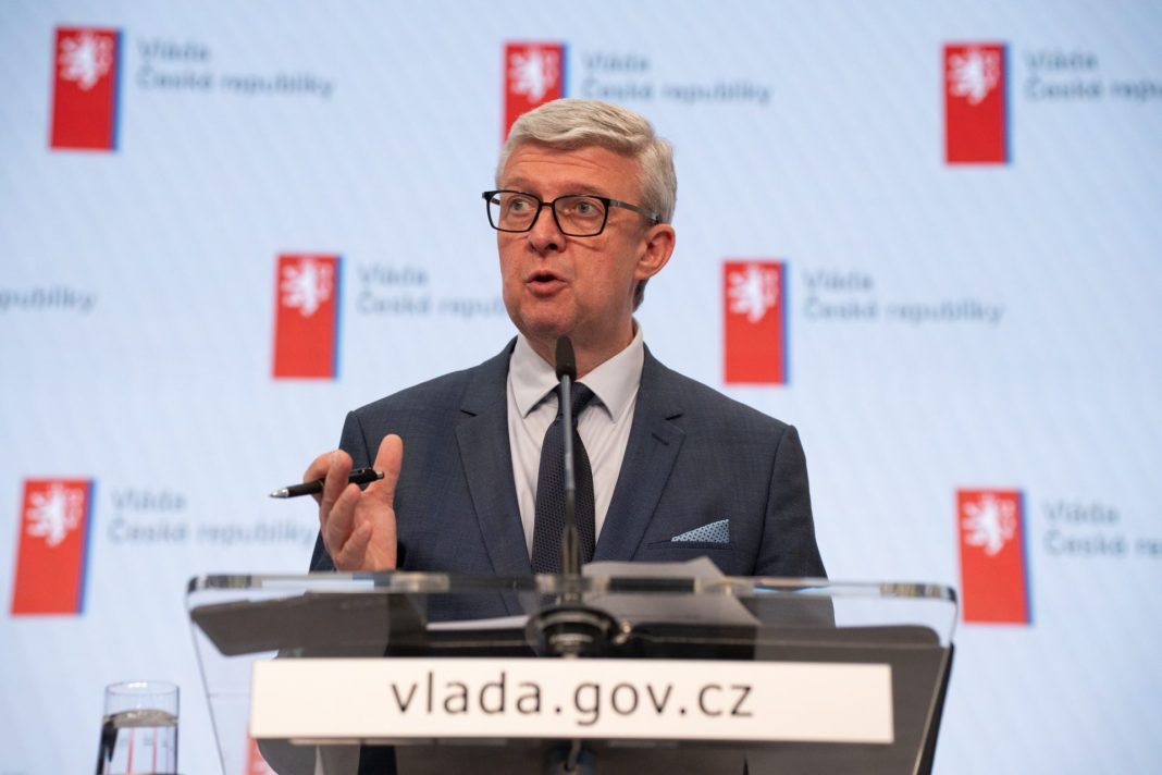 Ministr průmyslu a obchodu Karel Havlíček vystupuje u řečnického pultu před symbolem vlády České republiky