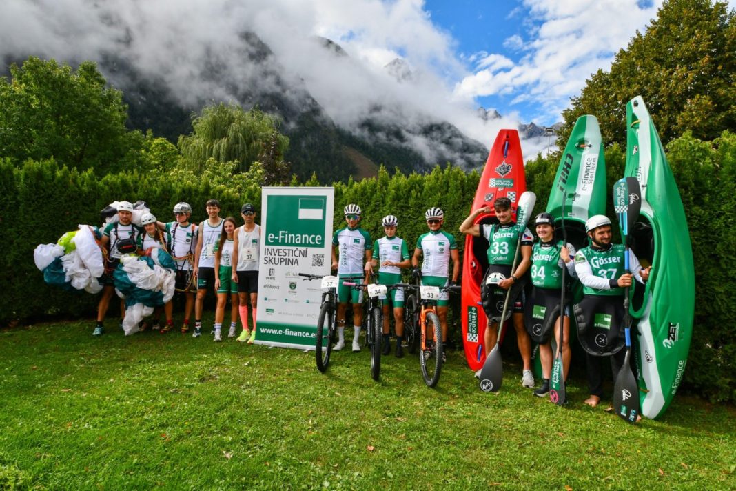 Členové e-Finance Sport Teamu pózují s koly, kajaky a paraglidingovým vybavením v horském prostředí