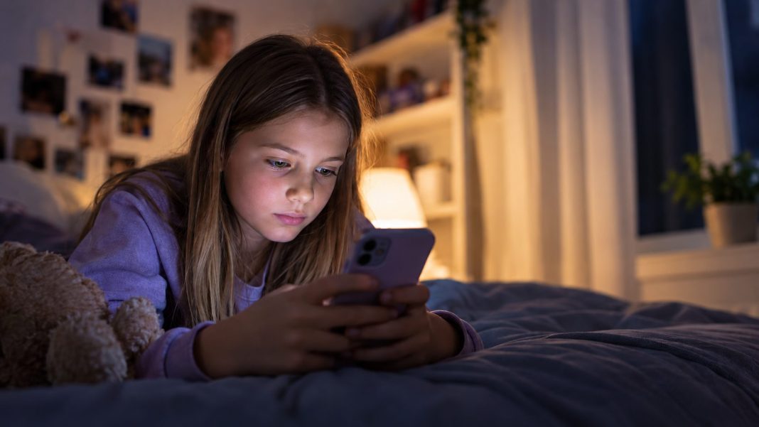 Dívka používající večer chytrý telefon v dětském pokoji