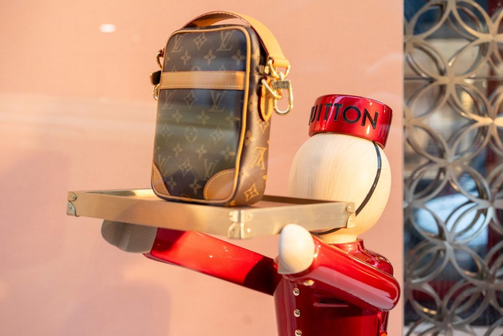Kabelka Louis Vuitton s monogramem vystavená na podnosu drženém červenou figurínou ve výloze