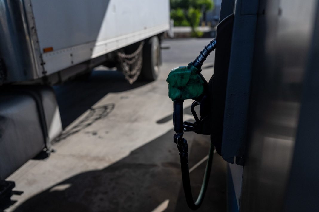 Zelená čerpací pistole u stojanu s nákladním vozem v pozadí
