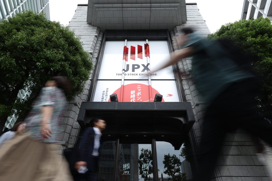 Vstup do budovy Tokyo Stock Exchange s logem JPX a procházejícími lidmi